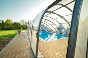 Grand abri de piscine haut en verre avec terrasse en bois
