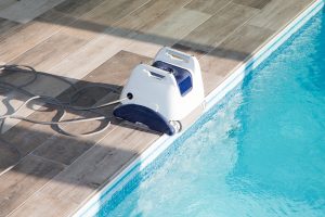 robot électrique de piscine blanc et bleu au bord de l'eau sur terrasse en bois avec cable