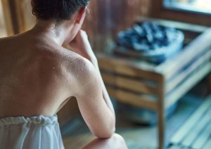 femme assise dans un sauna à vapeur avec pierres chaudes entrain de transpirer