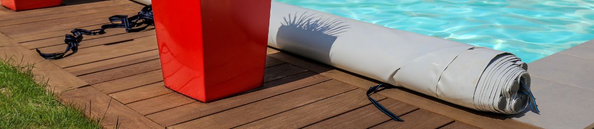 couverture à barres grise de piscine rangée sur le bord d'une piscine à côté de pots rouges