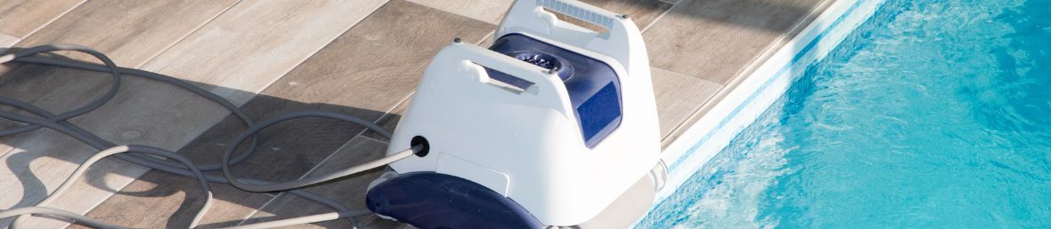 robot aspirateur de piscine blanc et bleu posé sur une margelle au bord de la piscine